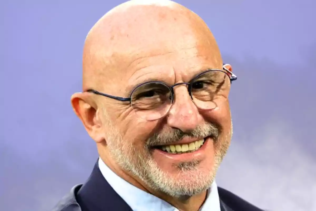 Home calb amb ulleres i barba somrient, amb americana i camisa clara davant d’un fons lila difuminat