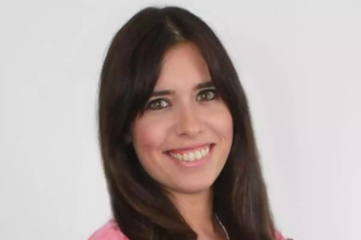 Dona jove de cabell llarg i fosc somrient davant d’un fons blanc