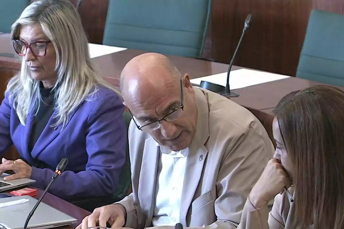 Tres personas sentadas en una sala de reuniones conversando y usando computadoras portátiles