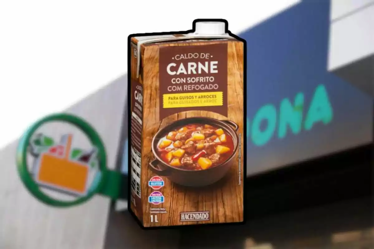 Envase de caldo de carne con sofrito de la marca Hacendado frente a un cartel borroso de supermercado