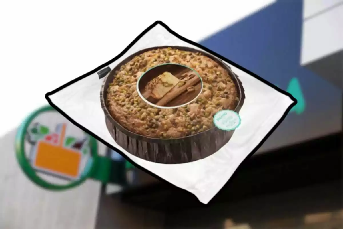 Pastel redondo con trozos de pistache en la parte superior dentro de un empaque transparente frente a una tienda