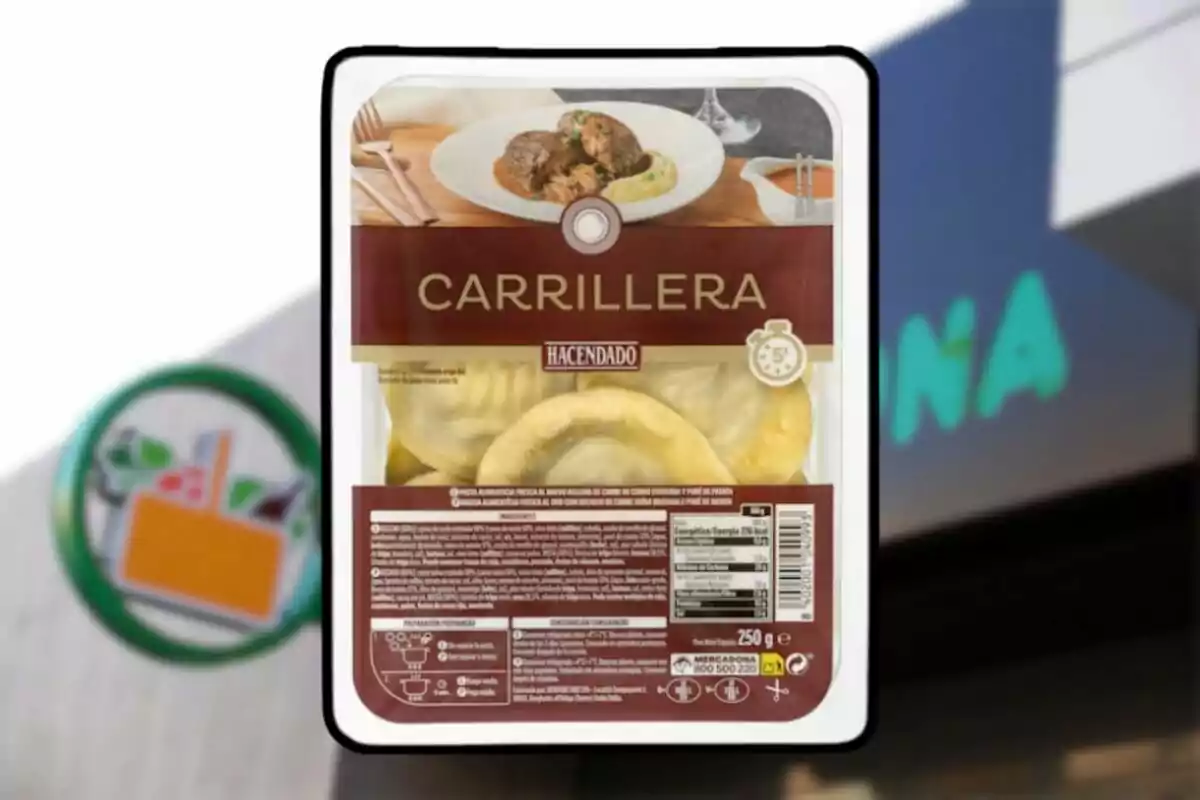 Envase de pasta rellena de carrillera de la marca Hacendado frente a un cartel de supermercado Mercadona desenfocado.