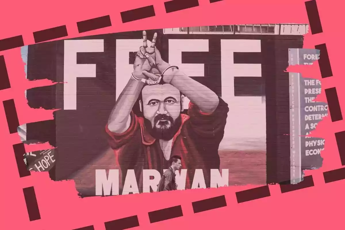 Mural d’un home amb barba i manilles aixecant les mans en senyal de victòria, que és Marwan Barghouti, amb la paraula FREE al darrere i una persona caminant davant de la pintura.