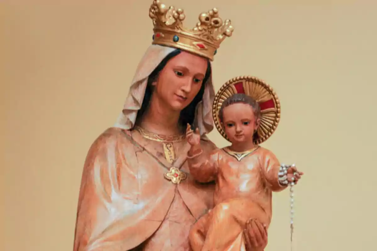 Escultura religiosa de una mujer con corona sosteniendo a un niño que lleva un rosario en la mano