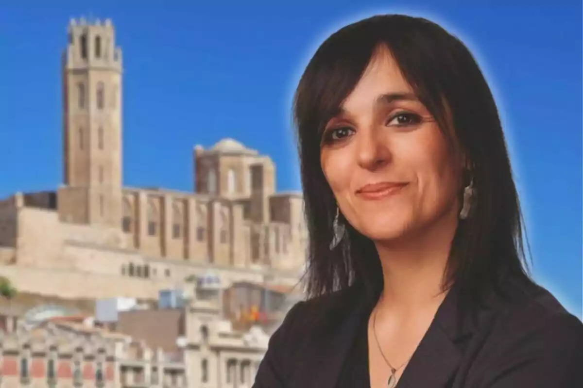 Mujer de cabello oscuro sonriendo con un edificio histórico de piedra al fondo y cielo azul