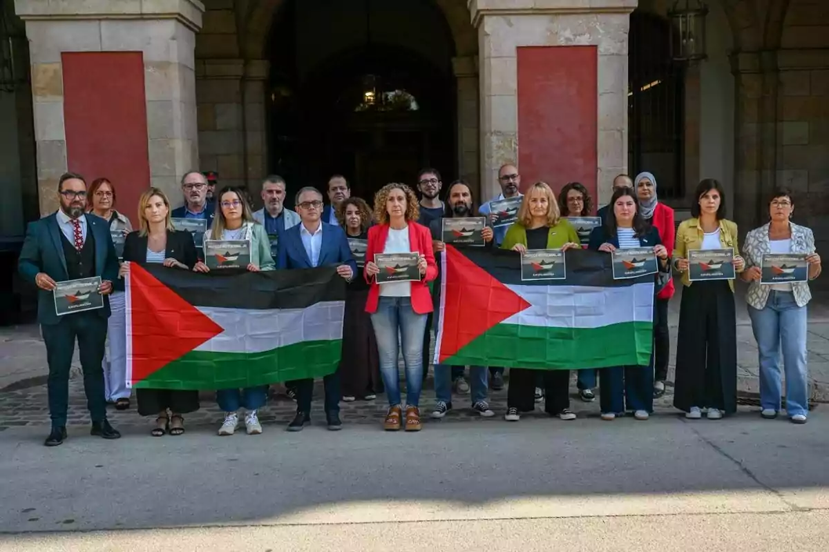 Un grup de persones posant davant d’un edifici sostenint banderes de Palestina i cartells en suport a la causa palestina
