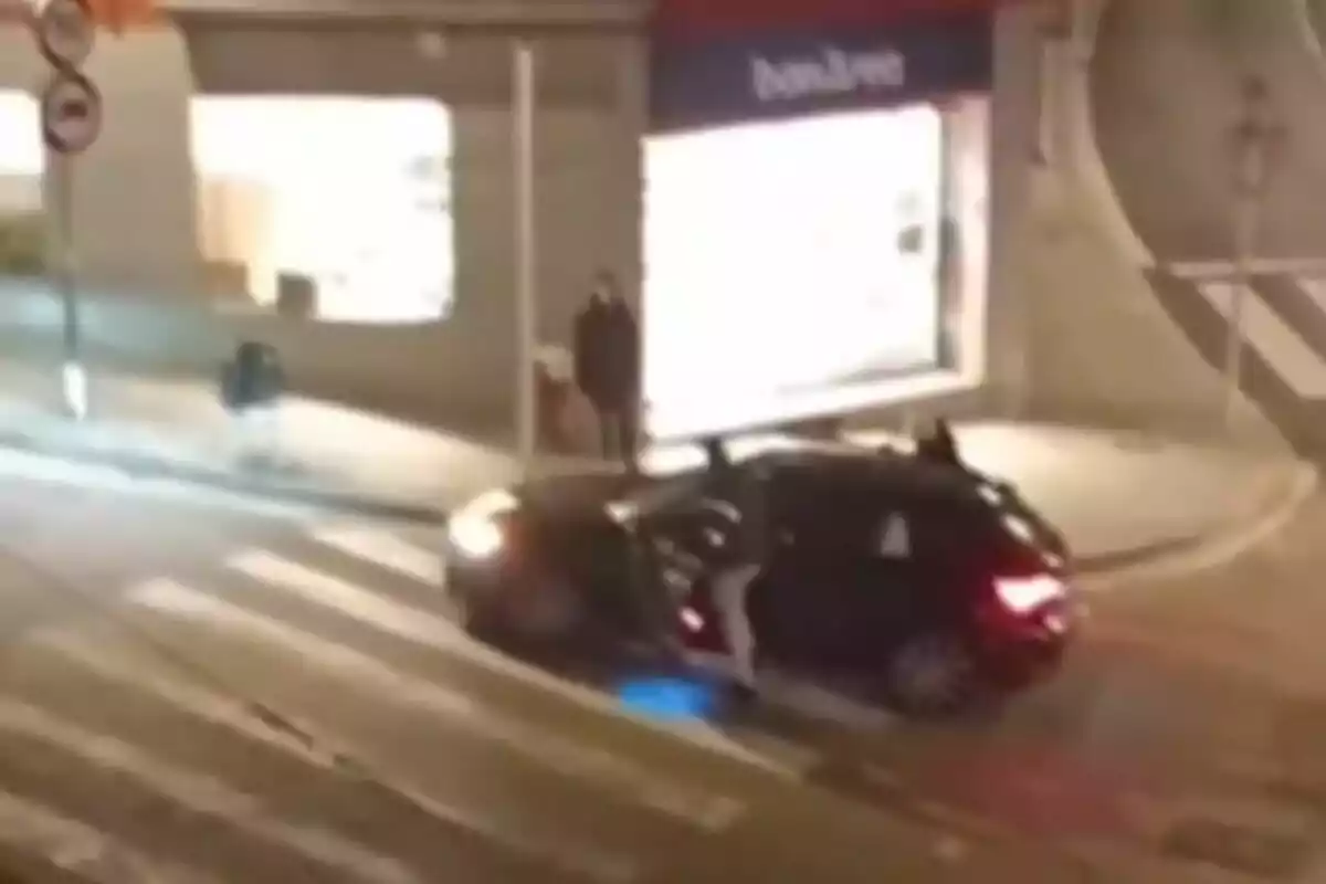 Un coche negro detenido en un paso de peatones durante la noche con una persona saliendo del vehículo y una tienda iluminada al fondo