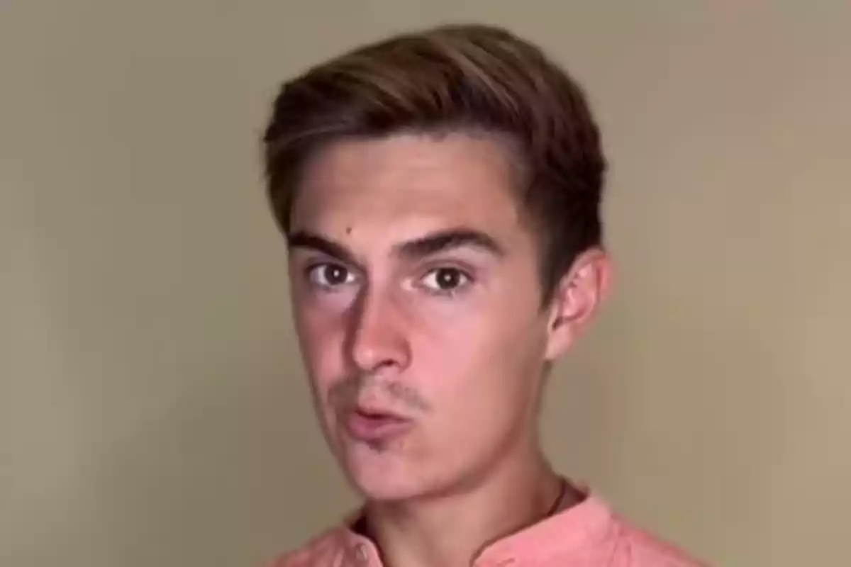 Jove de cabell curt i castany amb camisa rosa mirant cap a la càmera amb expressió seriosa