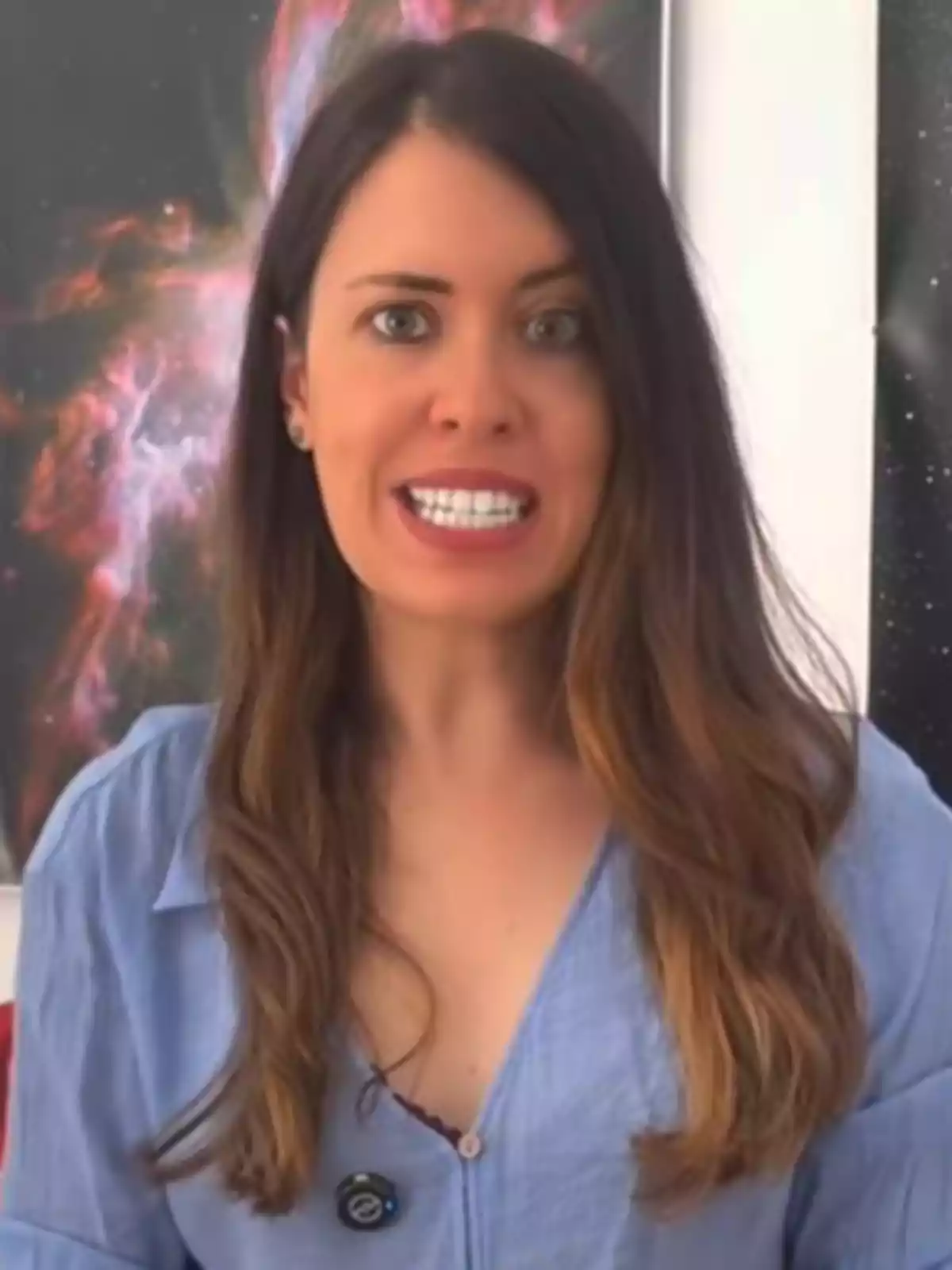 Dona de cabell llarg i castany amb camisa blau clar parlant davant d’un fons d’imatges espacials