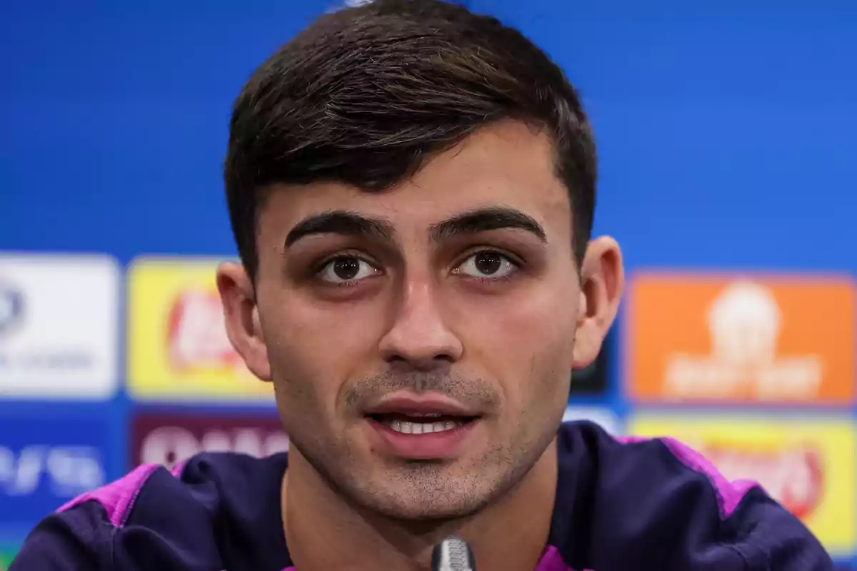 Pedri speaking in front of a microphone with a blue background and blurred logos