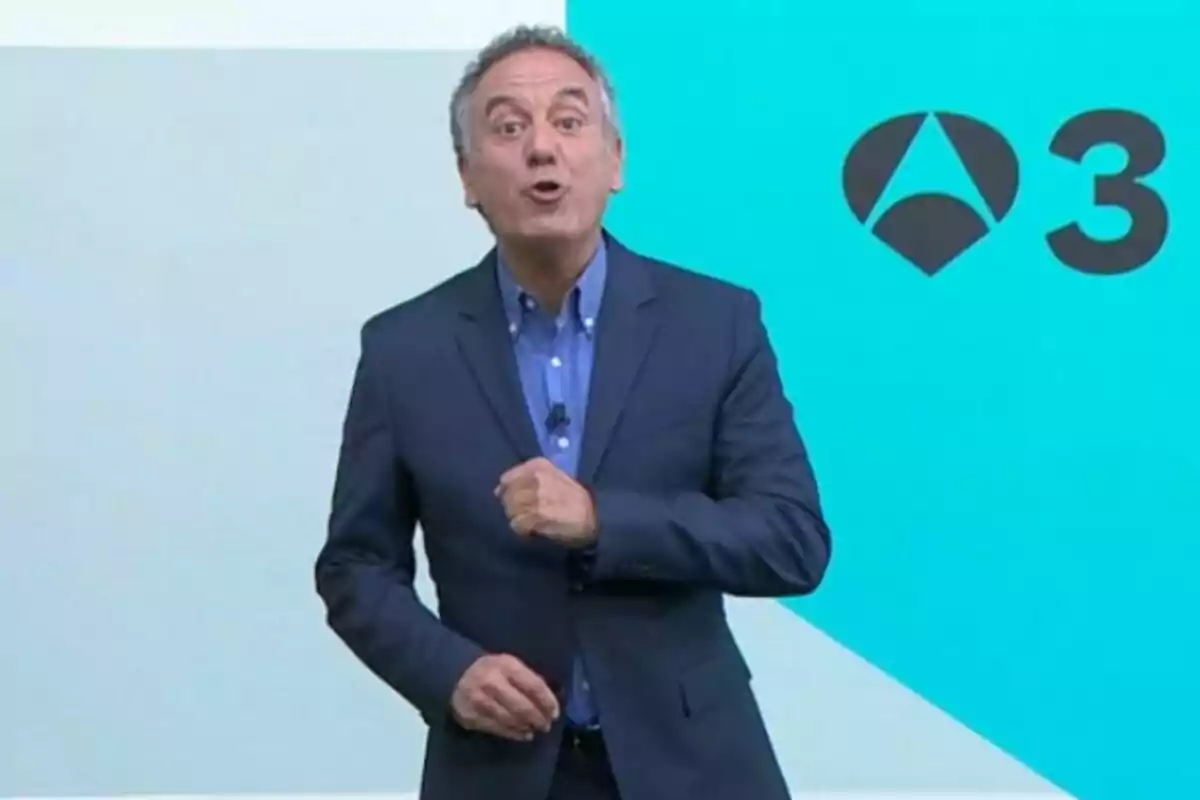 Pla mitjà de Roberto Brasero vestit amb un vestit blau parlant davant d’un fons blau clar amb el logotip d’Antena 3.