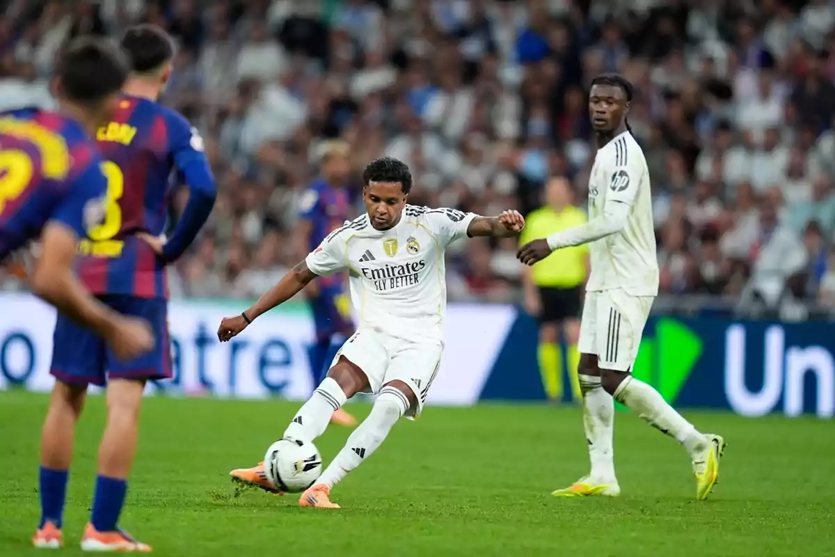 Jugador del Reial Madrid xutant la pilota durant un partit contra el Barcelona amb altres futbolistes observant la jugada al camp.