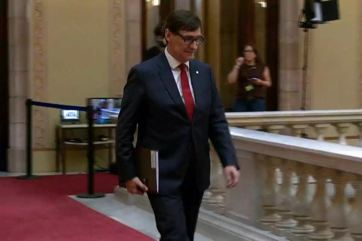 Home amb ulleres i vestit fosc caminant per un edifici elegant amb catifa vermella i barana blanca Home amb ulleres i vestit fosc caminant per un edifici elegant amb catifa vermella i barana blanca