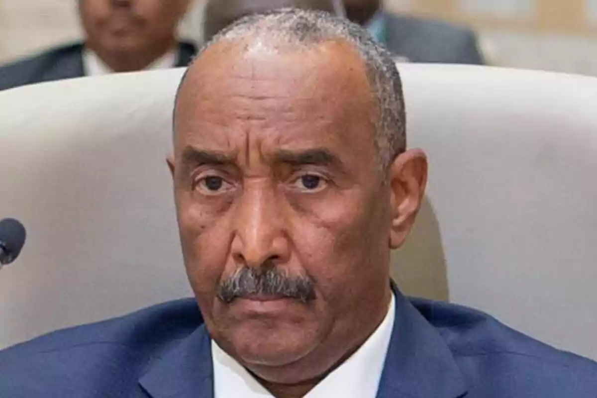 Primer plano de Abdel Fattah al-Burhan con bigote y cabello corto canoso vistiendo traje azul sentado en una silla blanca. Primer plano de Abdel Fattah al-Burhan con bigote y cabello corto canoso vistiendo traje azul sentado en una silla blanca.