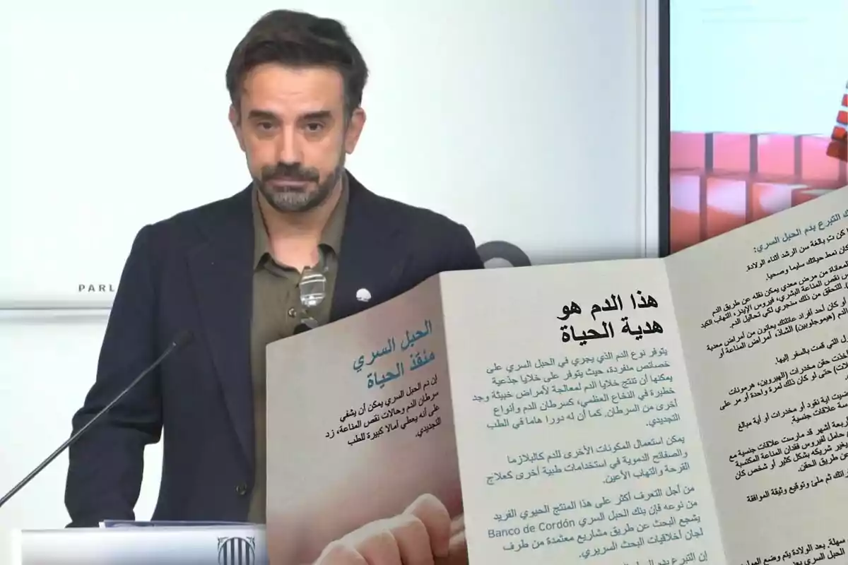 Un hombre de cabello corto y barba está de pie frente a un micrófono, mientras en primer plano se muestra un folleto abierto con texto en árabe sobre la donación de sangre.