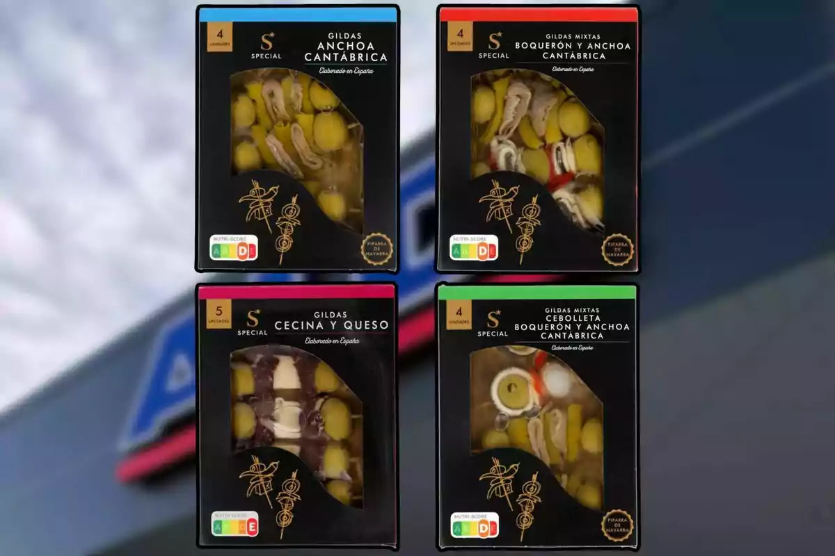 Cuatro cajas de gildas y pinchos variados en envases negros con ventana transparente, cada una con diferentes combinaciones de ingredientes como anchoa, boquerón, cecina, queso y cebolleta, sobre un fondo desenfocado. Cuatro cajas de gildas y pinchos variados en envases negros con ventana transparente, cada una con diferentes combinaciones de ingredientes como anchoa, boquerón, cecina, queso y cebolleta, sobre un fondo desenfocado.