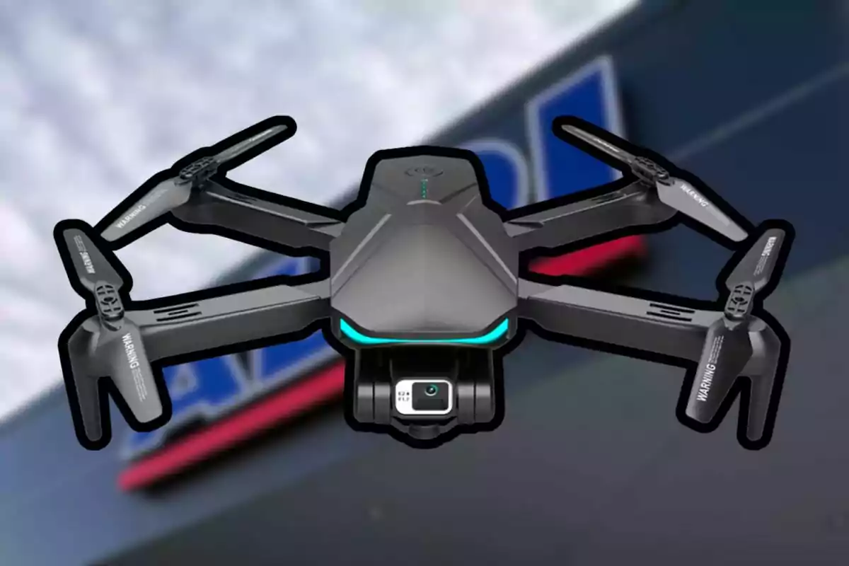 Un dron negre amb càmera vola davant d’un fons desenfocat d’un edifici amb lletres blaves i vermelles.