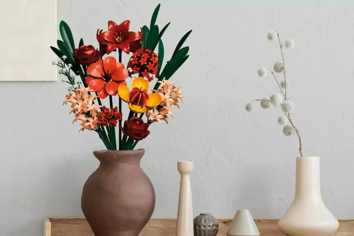 Ramo de flors de colors vius fetes amb peces de LEGO en un gerro marró sobre una taula de fusta al costat de diversos gerros decoratius en tons clars davant d’una paret gris clara