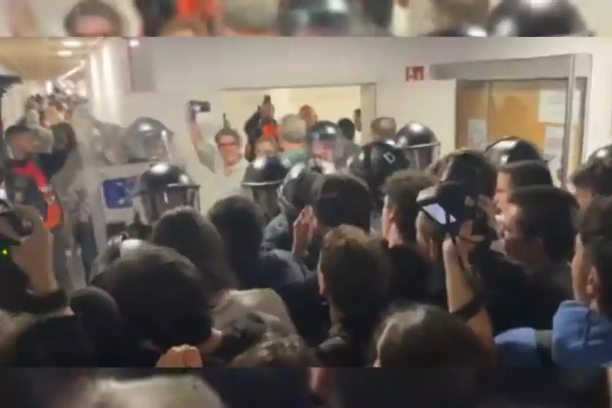 Un grupo de personas se enfrenta a policías antidisturbios en un pasillo mientras algunos observadores graban la escena con sus teléfonos móviles