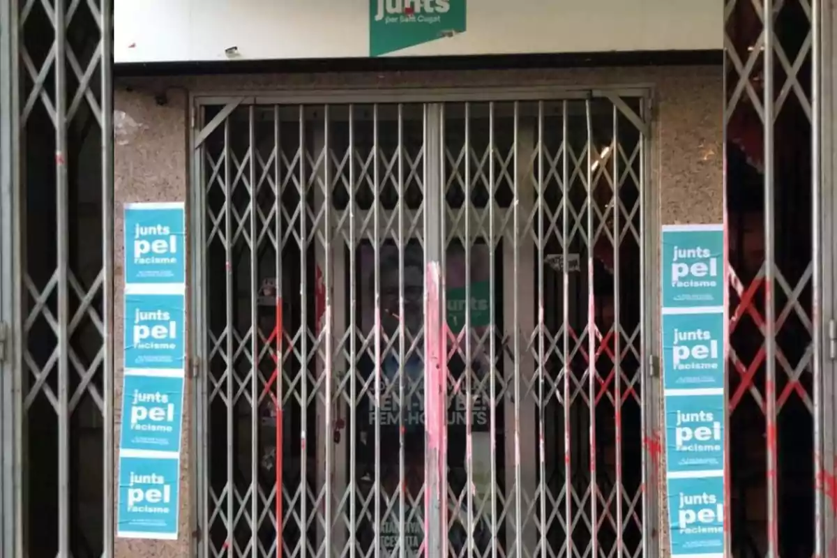 Porta metàl·lica tancada amb cartells blaus que diuen junts pel racisme enganxats als costats i un rètol de junts a la part superior