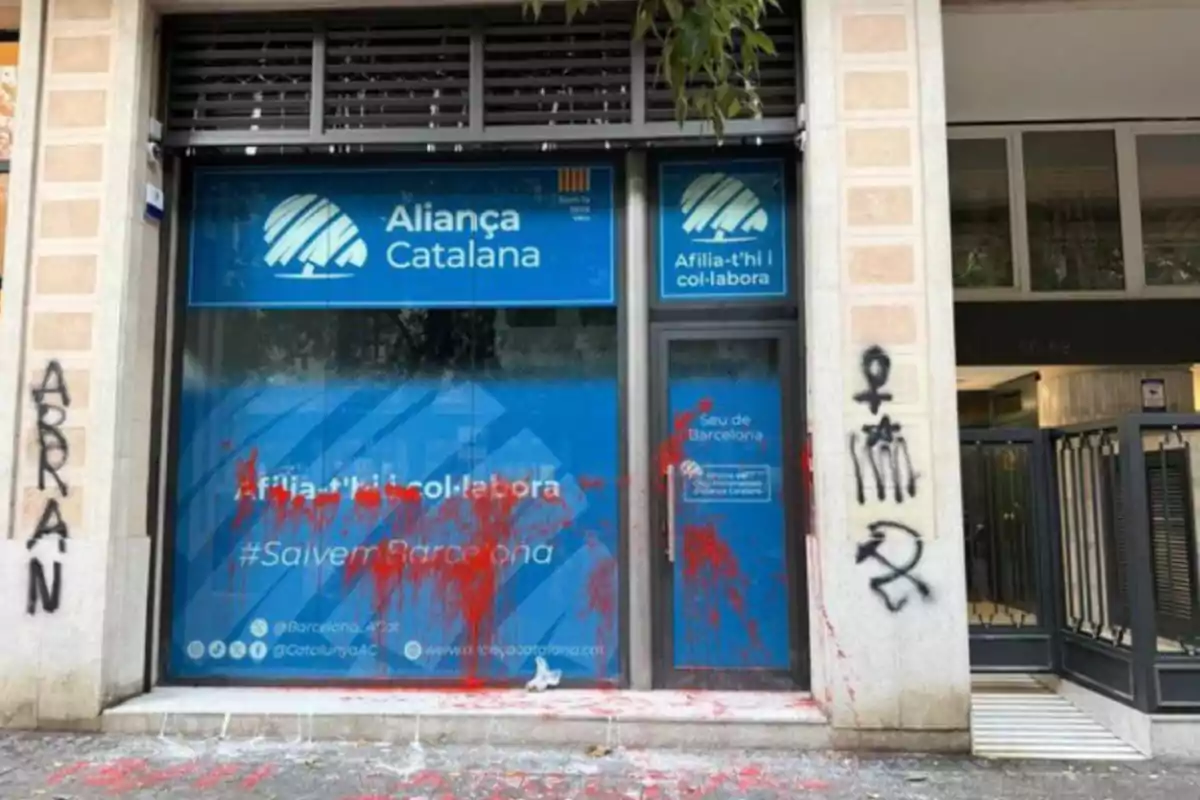Façana d’una oficina d’Aliança Catalana amb pintades i taques de pintura vermella als vidres i parets