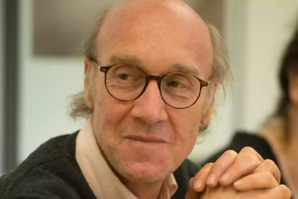 Hombre mayor con gafas redondas y expresión pensativa apoyando las manos entrelazadas