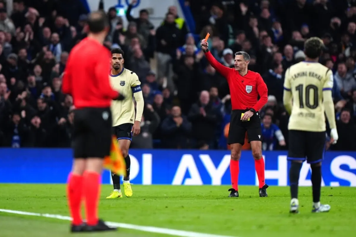 Referee showing a red card to a player during a soccer match while other players watch the decision