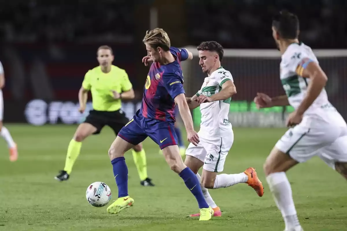 Dos futbolistas disputan el balón durante un partido mientras un árbitro observa la jugada en el fondo