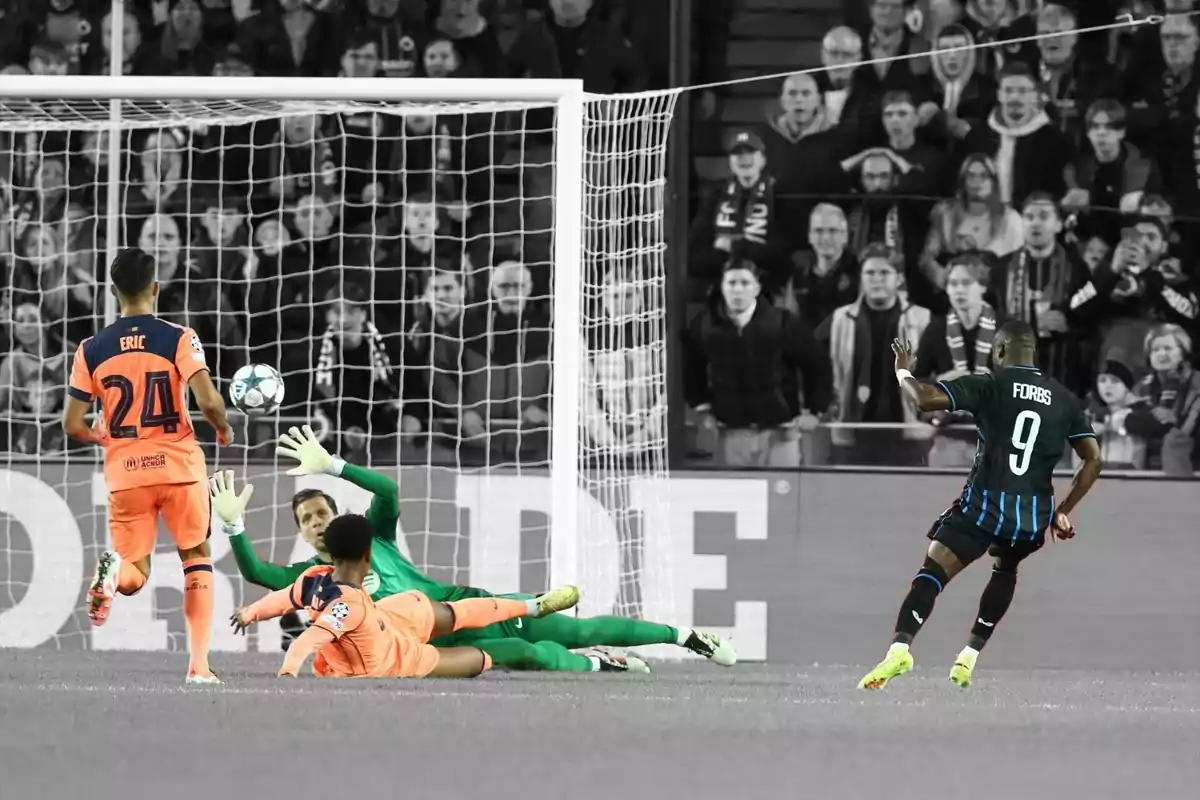 Un davanter amb el número 9 xuta a porteria mentre el porter i dos defenses intenten aturar la pilota en un partit de futbol amb la multitud de fons en blanc i negre i els jugadors en color. Un davanter amb el número 9 xuta a porteria mentre el porter i dos defenses intenten aturar la pilota en un partit de futbol amb la multitud de fons en blanc i negre i els jugadors en color.