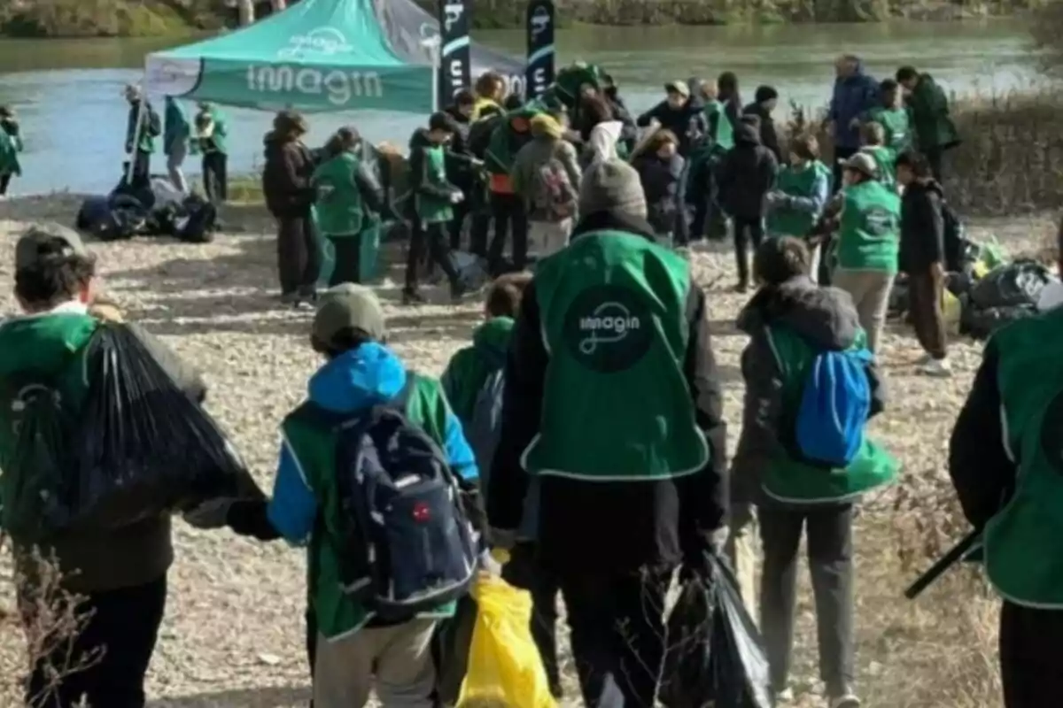 Grup de persones amb armilles verdes recollint escombraries al costat d’un riu durant una jornada de neteja ambiental