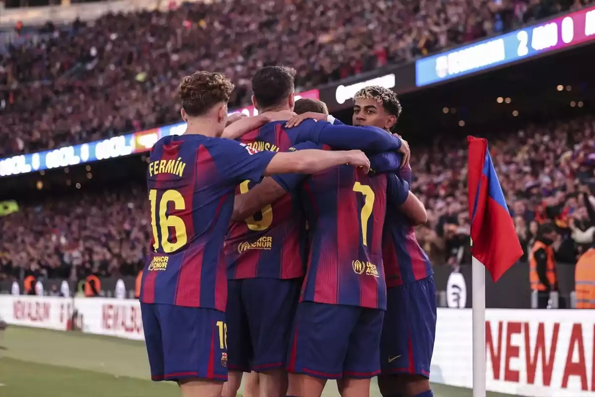 Jugadores del FC Barcelona celebran un gol abrazándose cerca del banderín de córner con la afición de fondo en el estadio