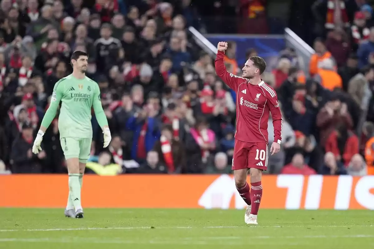Un jugador del Liverpool celebra aixecant el puny mentre un porter del Reial Madrid observa al camp durant un partit de futbol amb públic a les grades.