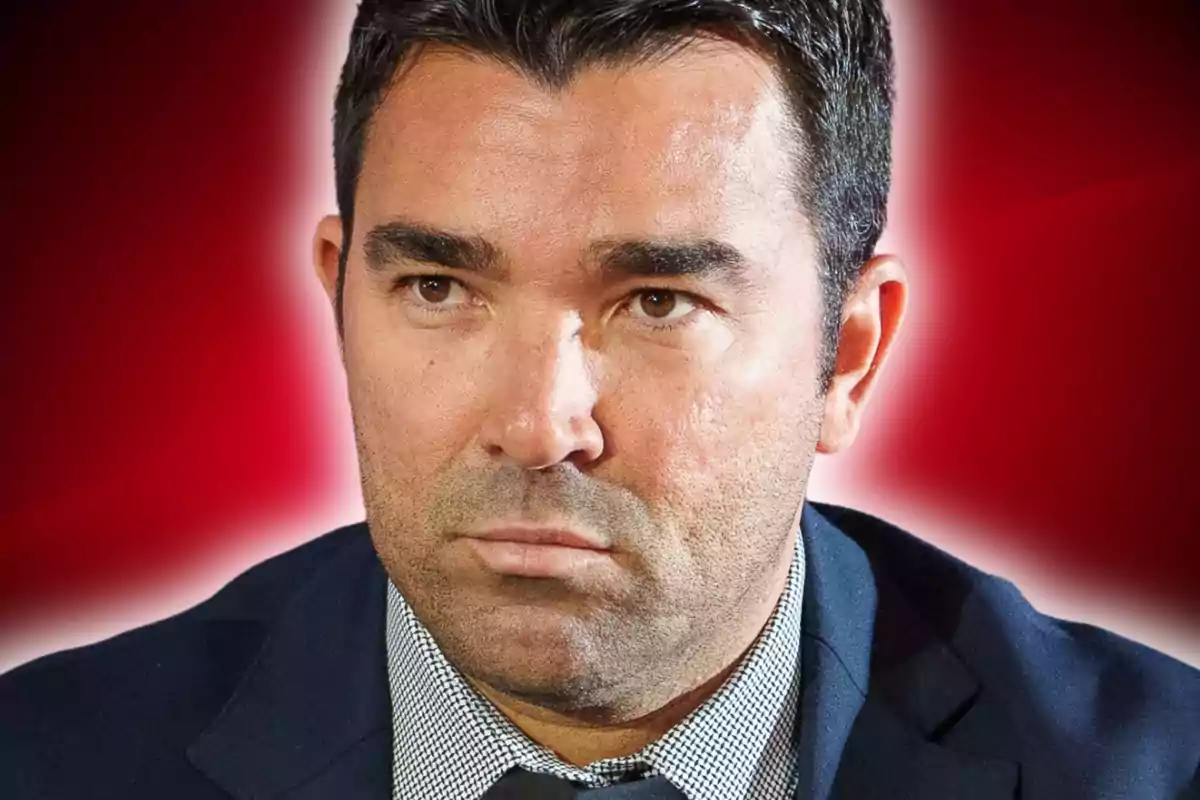 Hombre de cabello oscuro con expresión seria vistiendo saco y camisa frente a un fondo rojo difuminado