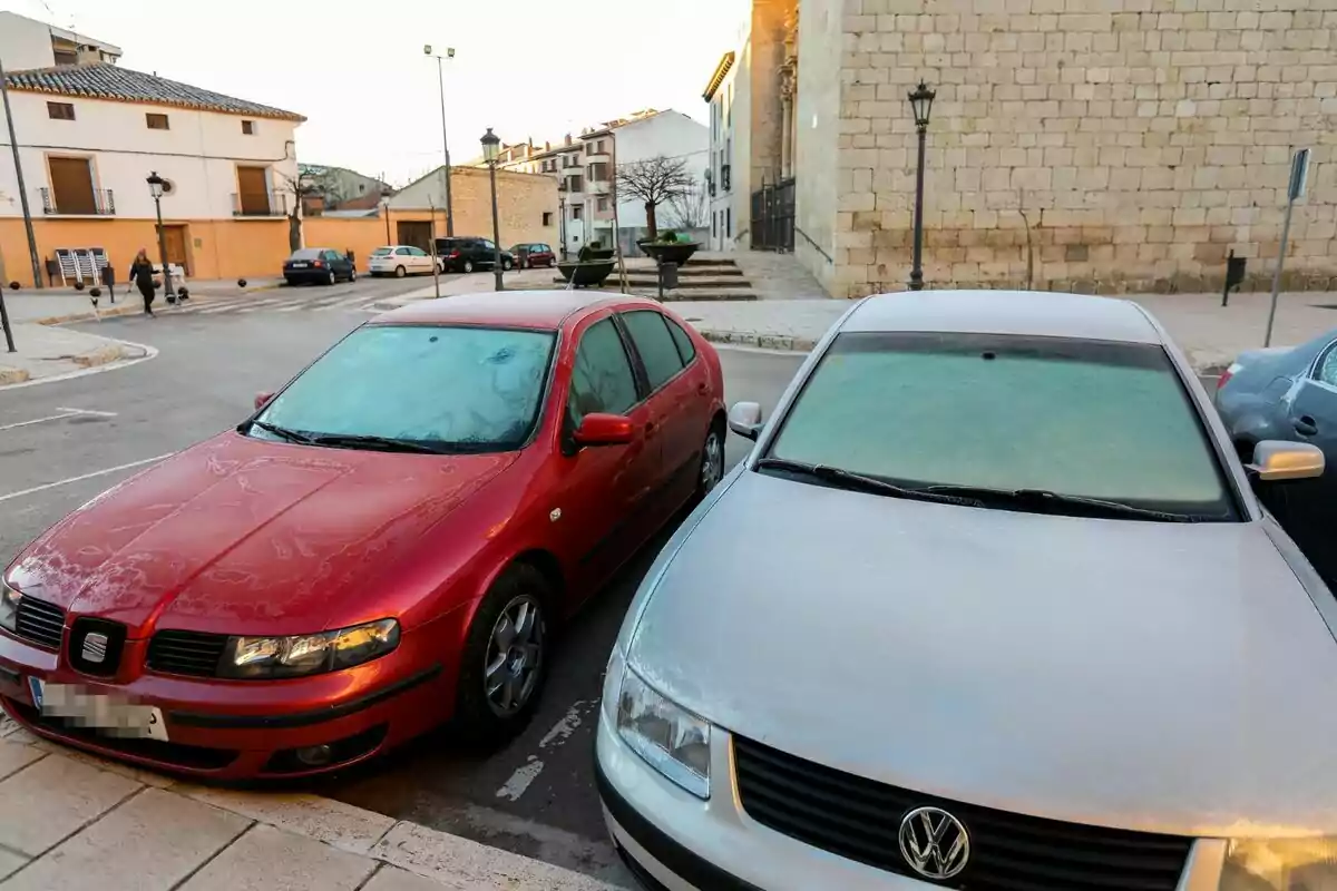 Dos cotxes estacionats amb els vidres coberts de gebre en un carrer d’un poble.
