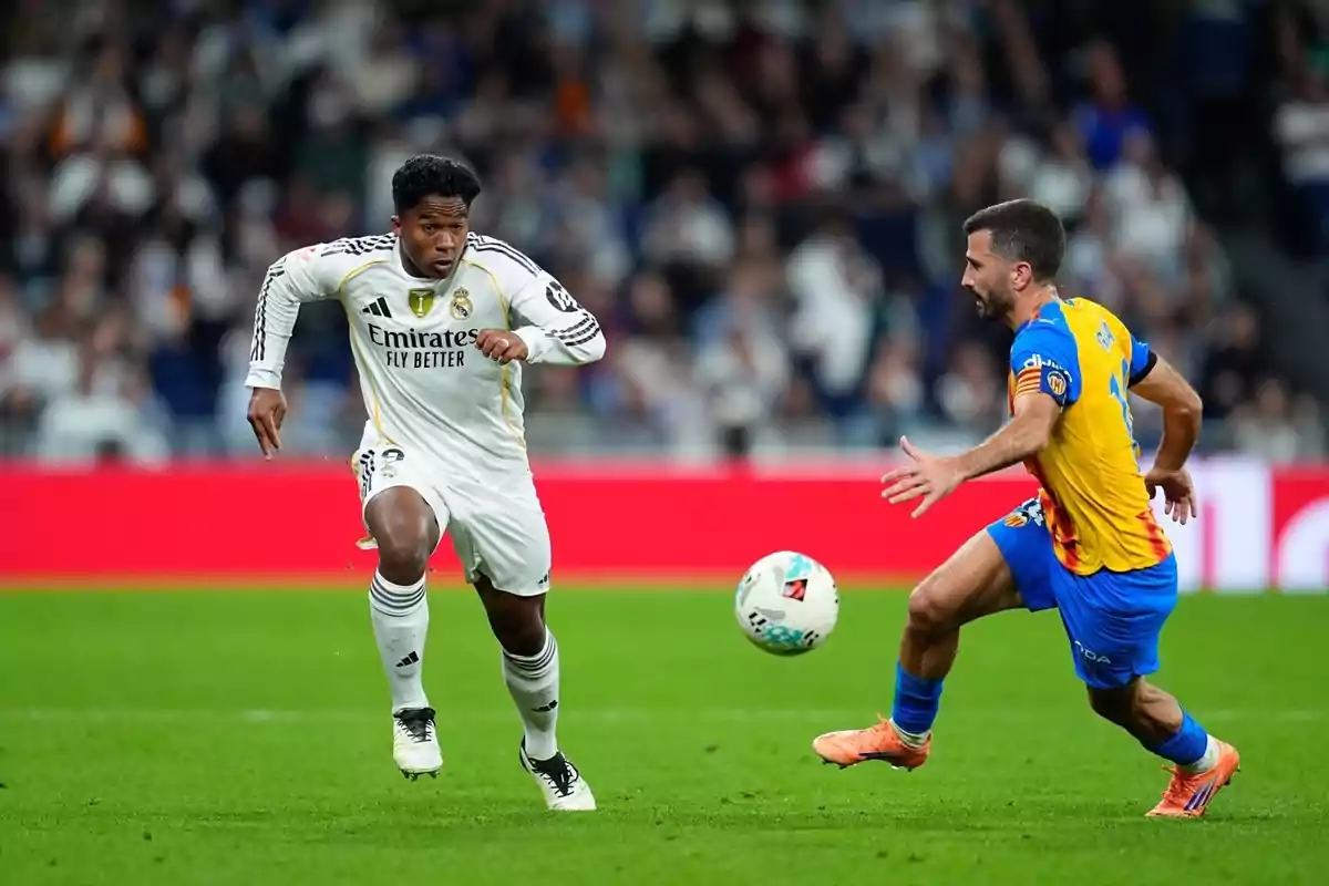 Dos futbolistes disputen la pilota durant un partit en un estadi ple d’espectadors