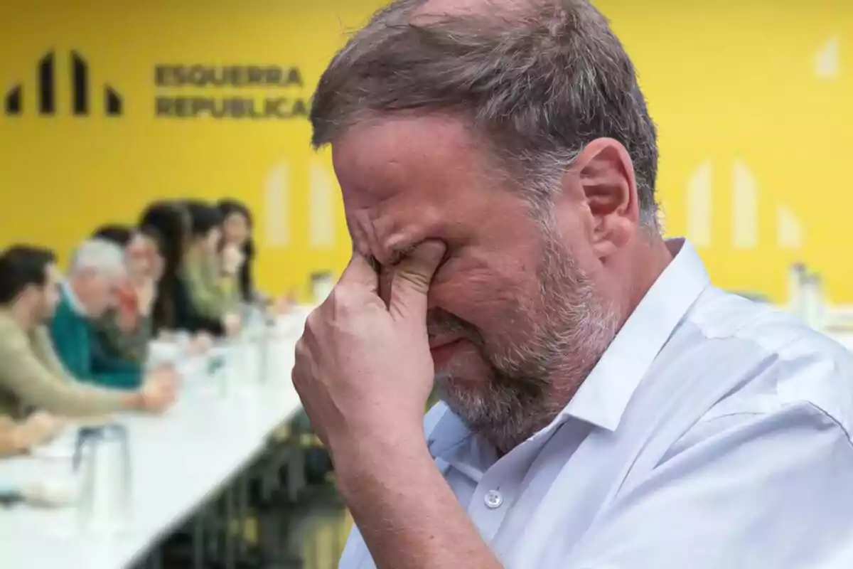 Hombre con gesto de preocupación frente a una reunión en una sala con fondo amarillo y el logo de Esquerra Republicana
