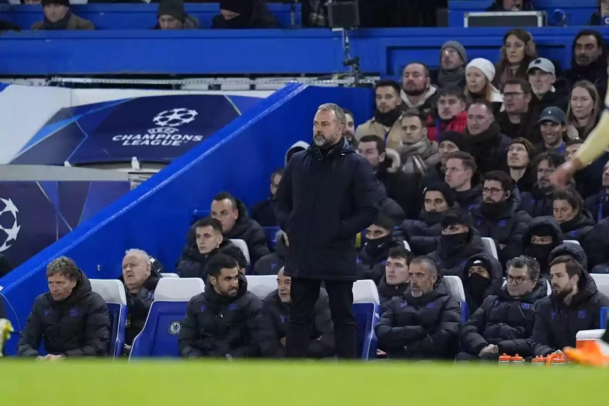 Entrenador de fútbol de pie frente al banquillo durante un partido de la Champions League con el público observando desde las gradas