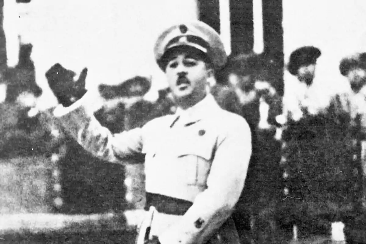 Francisco Franco con uniforme militar saludando con la mano derecha levantada frente a un grupo de personas desenfocadas.