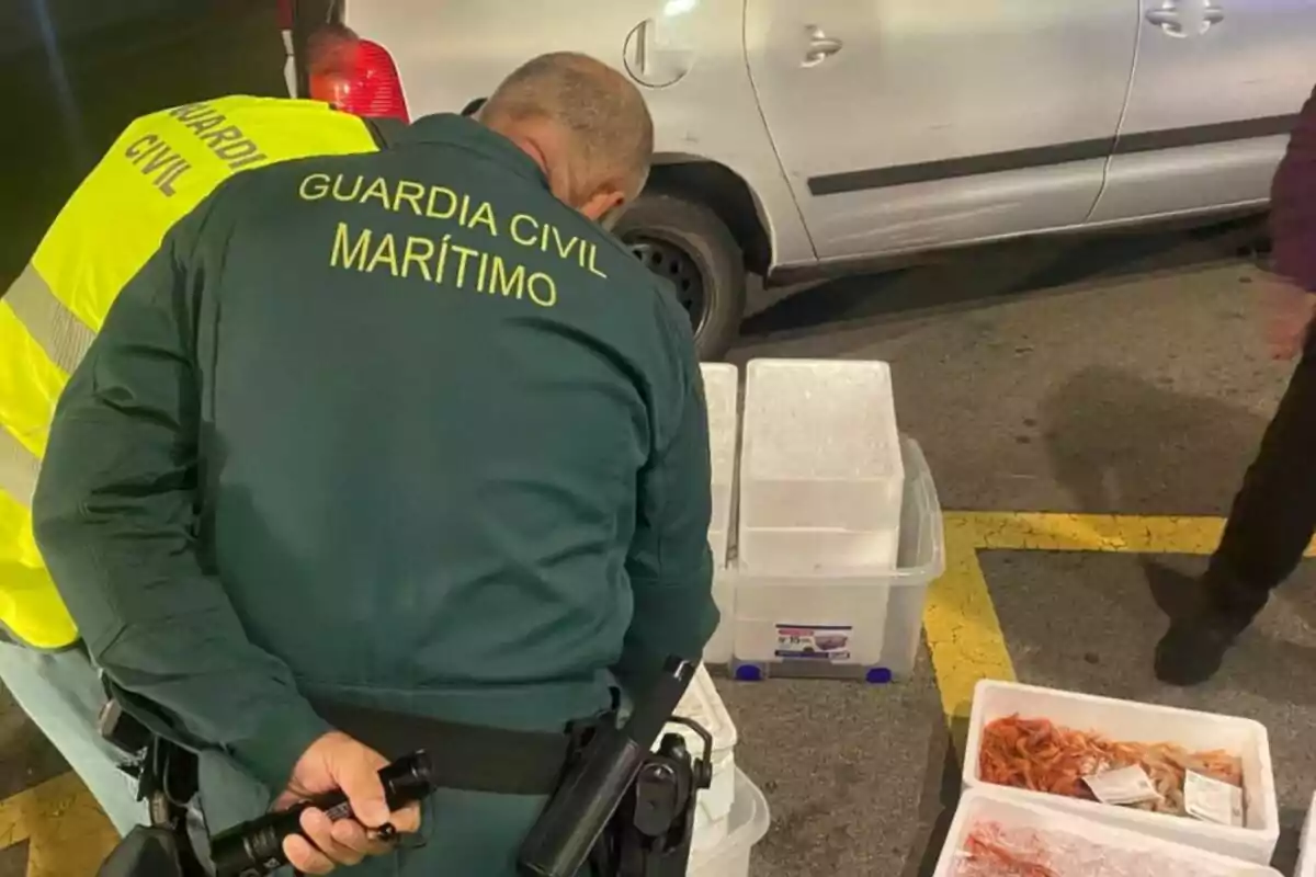 Dos agents de la Guàrdia Civil Marítima inspeccionen diverses caixes de plàstic amb marisc al costat d’un cotxe estacionat
