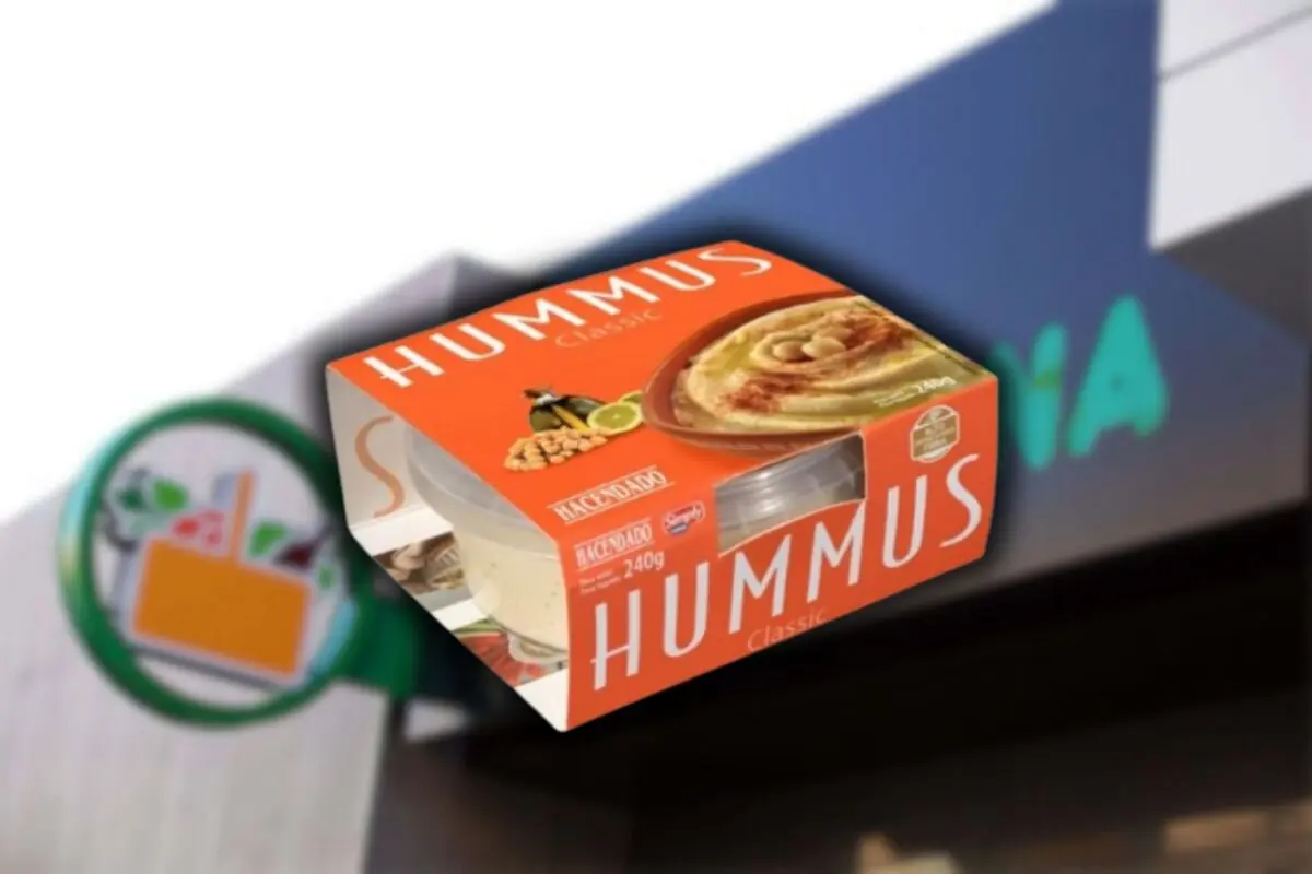 Envàs d’hummus clàssic de la marca Hacendado davant d’un cartell borros de supermercat Envàs d’hummus clàssic de la marca Hacendado davant d’un cartell borros de supermercat