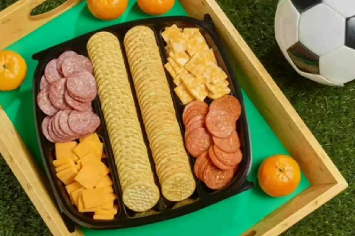 Tray with salty crackers, slices of salami, slices of pepperoni, cubes of yellow cheese and marbled cheese from Sam's Club, served with mandarins and a soccer ball on artificial grass. Tray with salty crackers, slices of salami, slices of pepperoni, cubes of yellow cheese and marbled cheese from Sam's Club, served with mandarins and a soccer ball on artificial grass.