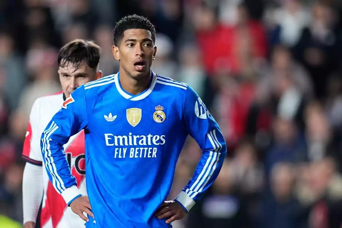 Futbolista del Reial Madrid amb uniforme blau durant un partit, amb un jugador rival al fons i públic desenfocat a les grades
