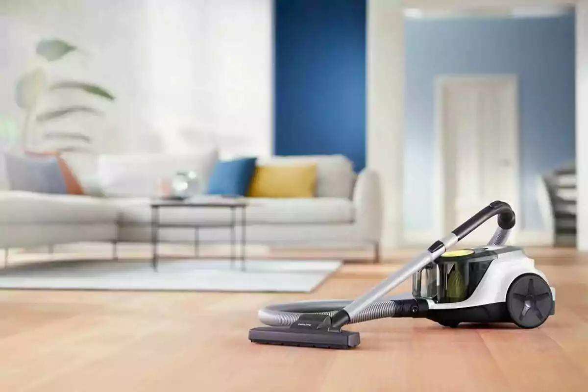 Aspiradora sobre un piso de madera en una sala moderna con sofá y cojines de colores al fondo