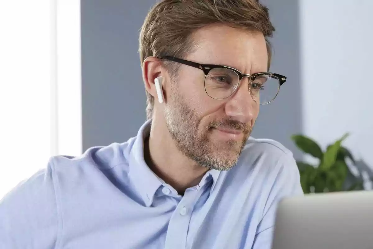 Home amb ulleres i auriculars sense fils treballant davant d’un ordinador portàtil