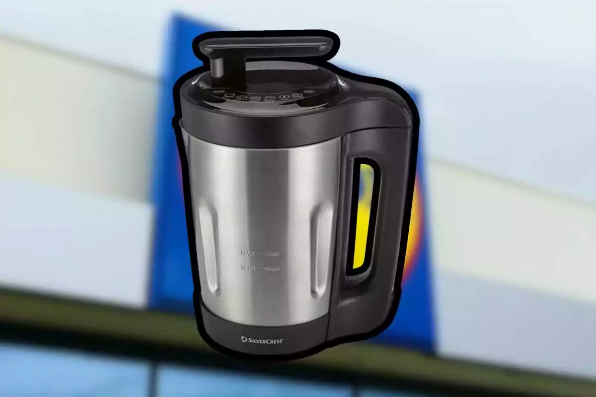 Processador d’aliments platejat i negre amb una nansa gran sobre un fons desenfocat de colors blau, blanc i groc