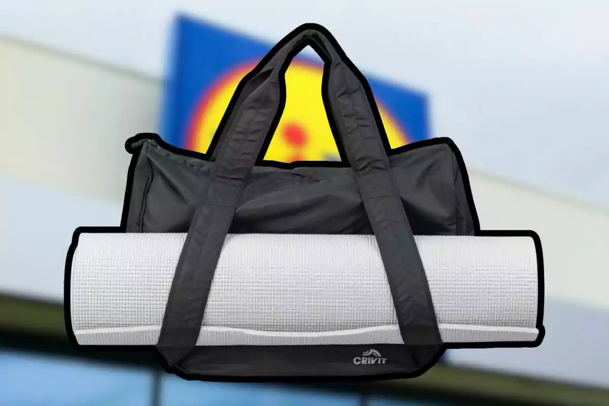 Bolsa deportiva negra con asas largas y tapete enrollado de color blanco al frente, con el logo Crivit, sobre un fondo desenfocado de una tienda.
