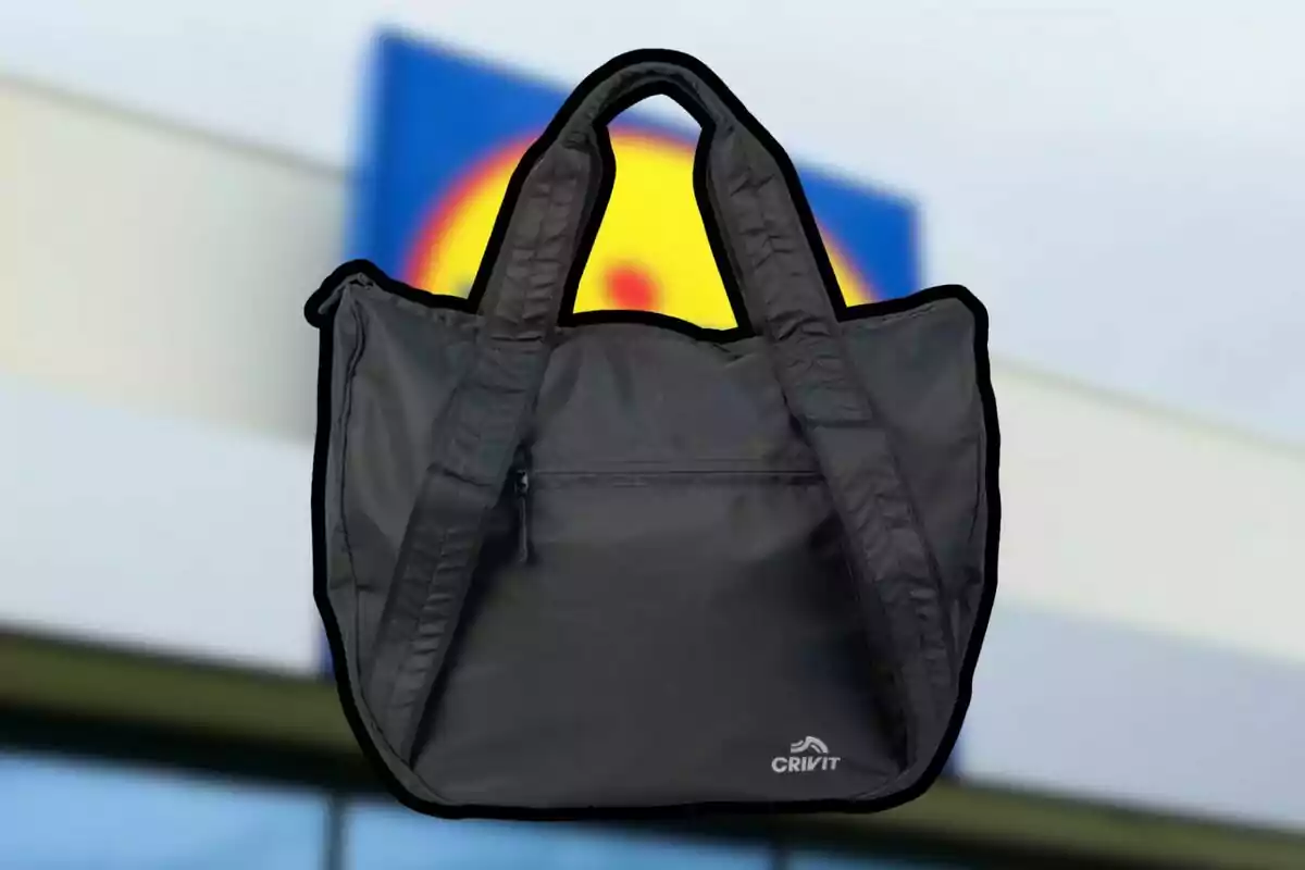 Bolsa deportiva negra de la marca Crivit con asas anchas y un bolsillo frontal con cierre, al fondo se distingue un letrero borroso de colores azul y amarillo.
