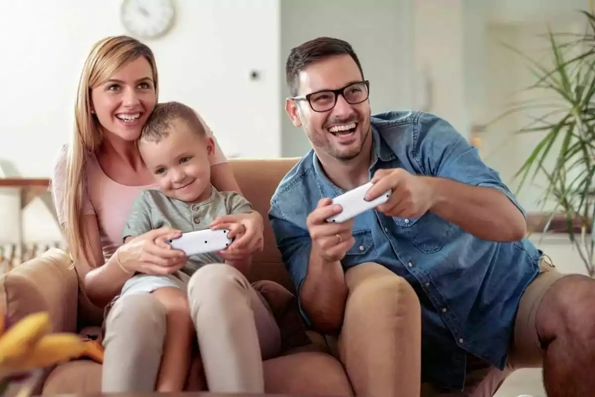 Familia sonriente sentada en un sofá jugando videojuegos juntos Familia sonriente sentada en un sofá jugando videojuegos juntos