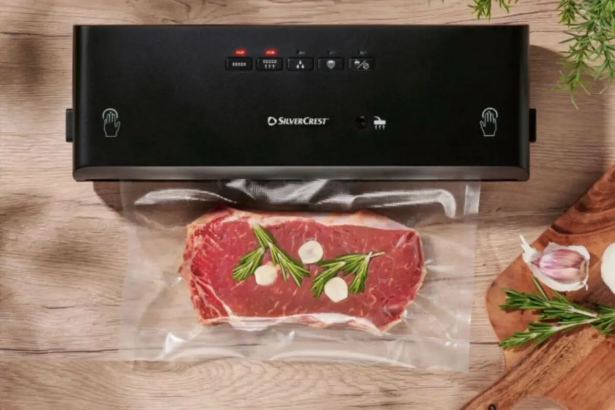 Vacuum packaging machine sealing a steak with sprigs of rosemary and slices of garlic on a wooden table Vacuum packaging machine sealing a steak with sprigs of rosemary and slices of garlic on a wooden table