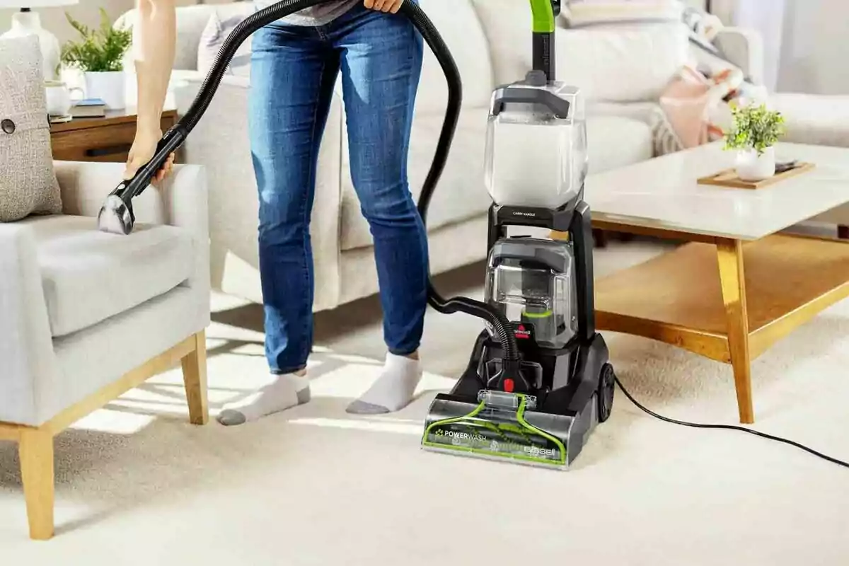 Persona utilitzant una aspiradora per netejar un sofà en una sala moderna i lluminosa